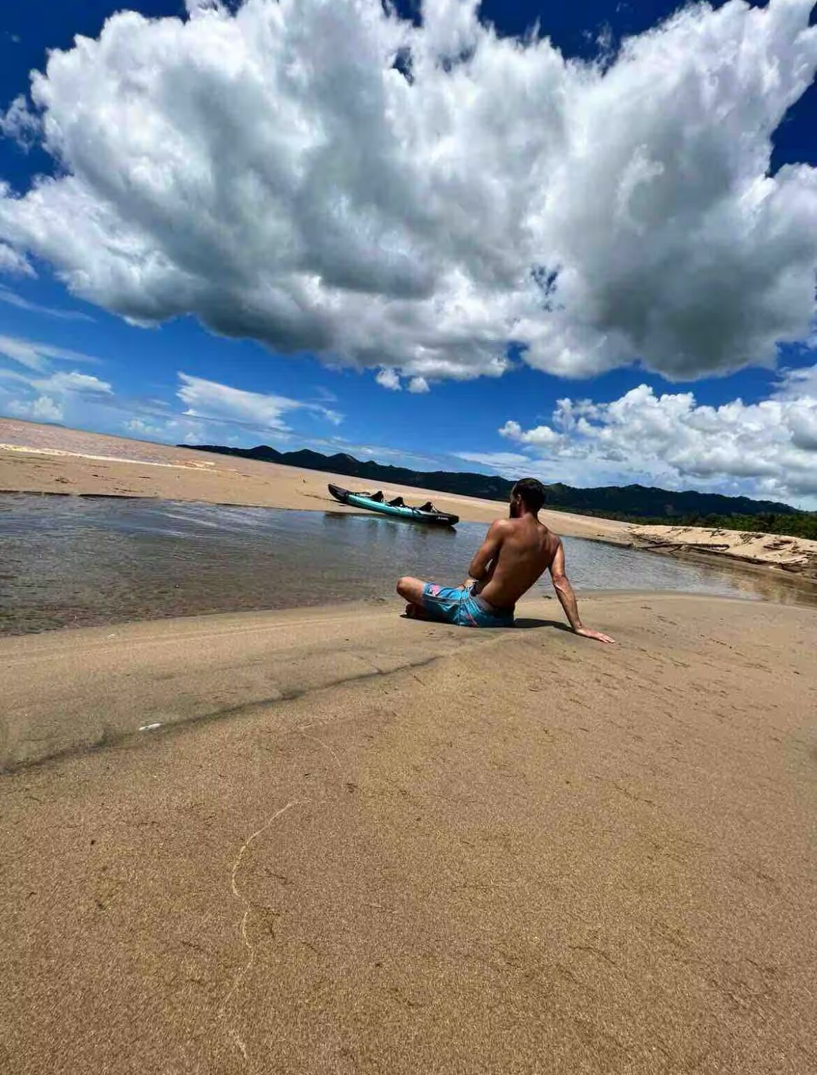 A sandy beach with a clear sky and a kayak in the water.