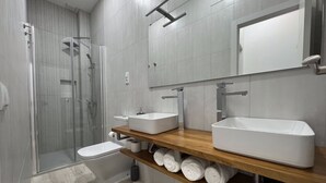 Ett modernt badrum med en duschavdelning med glasväggar, en toalett och två handfat placerade på en bänkskiva i trä.