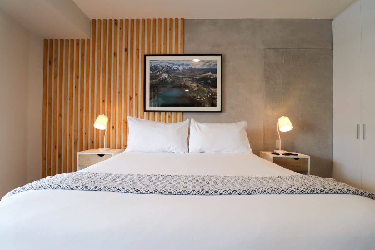 A modern bedroom with a large bed, wooden panel wall, and a framed landscape painting.