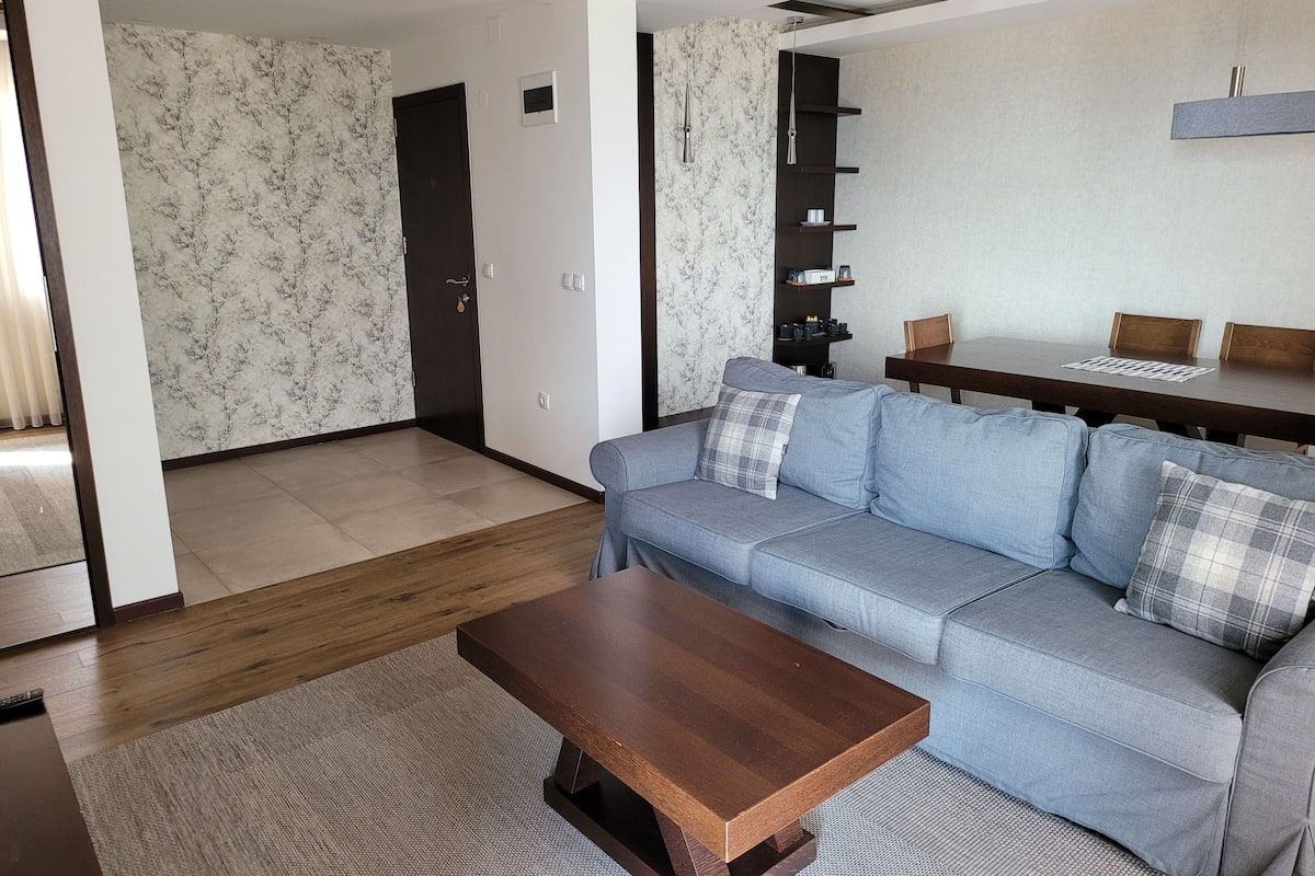 A modern living room with a grey sofa, a wooden coffee table, and a dining area with a dark wooden table.