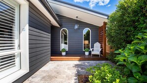 Una casa moderna con facciata grigia, un portico coperto con due vasi di piante e una poltrona Adirondack bianca.