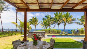 An outdoor dining area with a view of the ocean, palm trees, and a pool.
