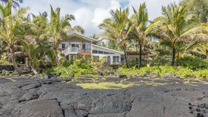 A house with a balcony, surrounded by palm trees and volcanic rocks.