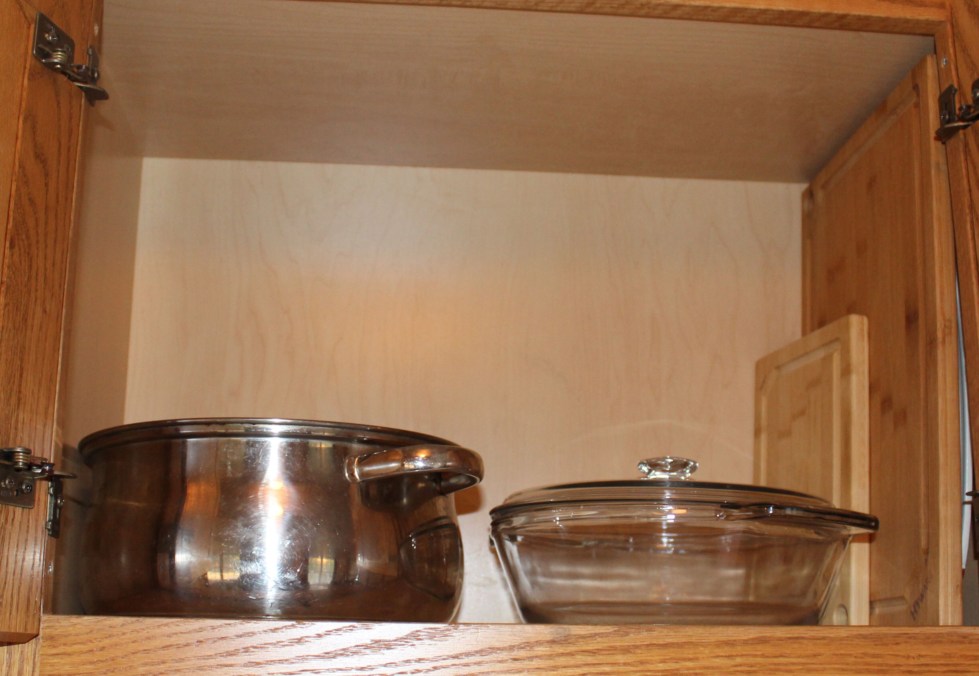 A wooden cabinet with a metal pot and a glass bowl inside.