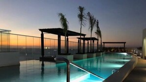 Ein Swimmingpool mit Glasbarriere, Palmen und Blick auf den Sonnenuntergang.