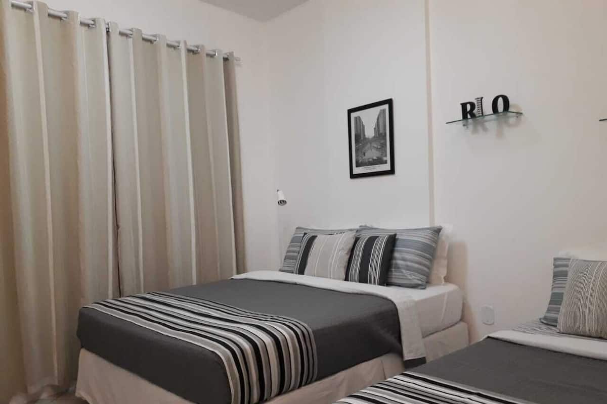 A bedroom with a bed, a bedside table, a chair, a curtain, a wall-mounted shelf with a picture, and a wall-mounted sign.