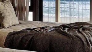 A hotel room with a bed, a large window, and a view of the ocean. - Seehuis (Yzerfontein)
