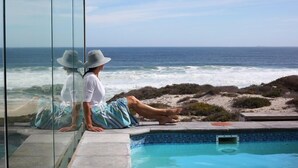 A poolside view with a clear ocean view, a glass barrier, and a sandy beach area. - Seehuis (Yzerfontein)