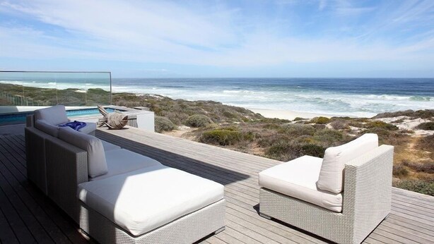 A deck with two white wicker sofas and a pool, overlooking a beach with waves and dunes. - Seehuis (Yzerfontein)