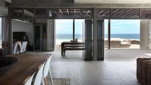 A modern interior with a dining area, a kitchen, and a view of the ocean. - Seehuis (Yzerfontein)
