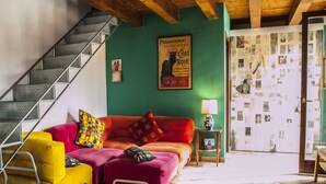 A living room with a staircase, a red sofa, a yellow armchair, and a green wall with a poster.