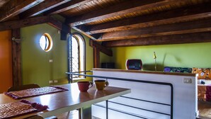 A rustic kitchen with wooden beams, a dining table with placemats, and a window with a view.