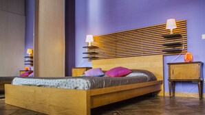 A modern bedroom with a wooden bed, purple walls, and a built-in shelf with a lamp.
