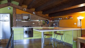 A kitchen with a wooden ceiling, a stainless steel refrigerator, a stove, and a sink. There are stools and a trash bin.