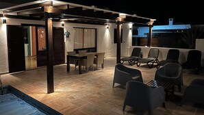 Een terras buiten met een zwembad, een eettafel met stoelen en zitmeubels.