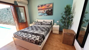 Een slaapkamer met een bed, nachtkastjes, een wandtelevisie, een potplant en uitzicht op het buiten.