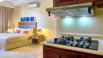 A hotel room with a bed, bedside table, lamp, and a kitchenette with a stove.