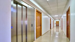 Een lange, goed verlichte gang met meerdere liften en houten deuren, die leidt naar een kamer met nummer 302.