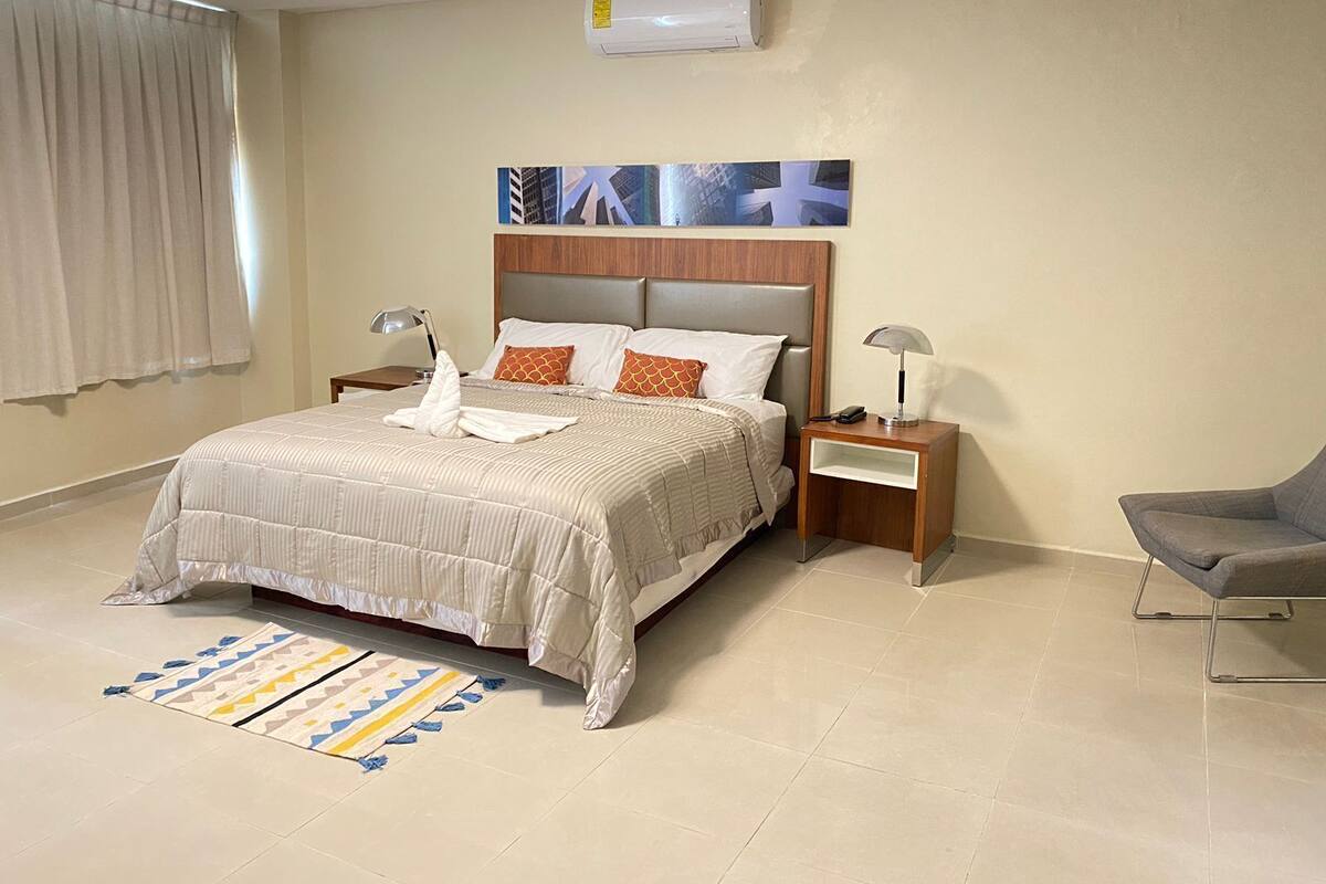 Une chambre d’hôtel comprenant un lit, des tables de chevet, une chaise, un tapis et un appareil de climatisation.