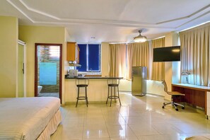 A hotel room with a bed, a desk with two stools, a TV, and a window with curtains. - Hotel Casa Libertad (Santo Domingo)