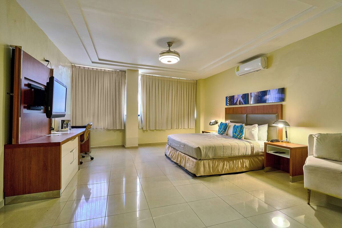 Une chambre d’hôtel comprenant un lit, une table de chevet, une lampe, une télévision, un bureau et des rideaux.