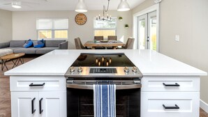 A modern kitchen with a central island, white cabinetry, a built-in oven, and a dining area with a table and chairs.