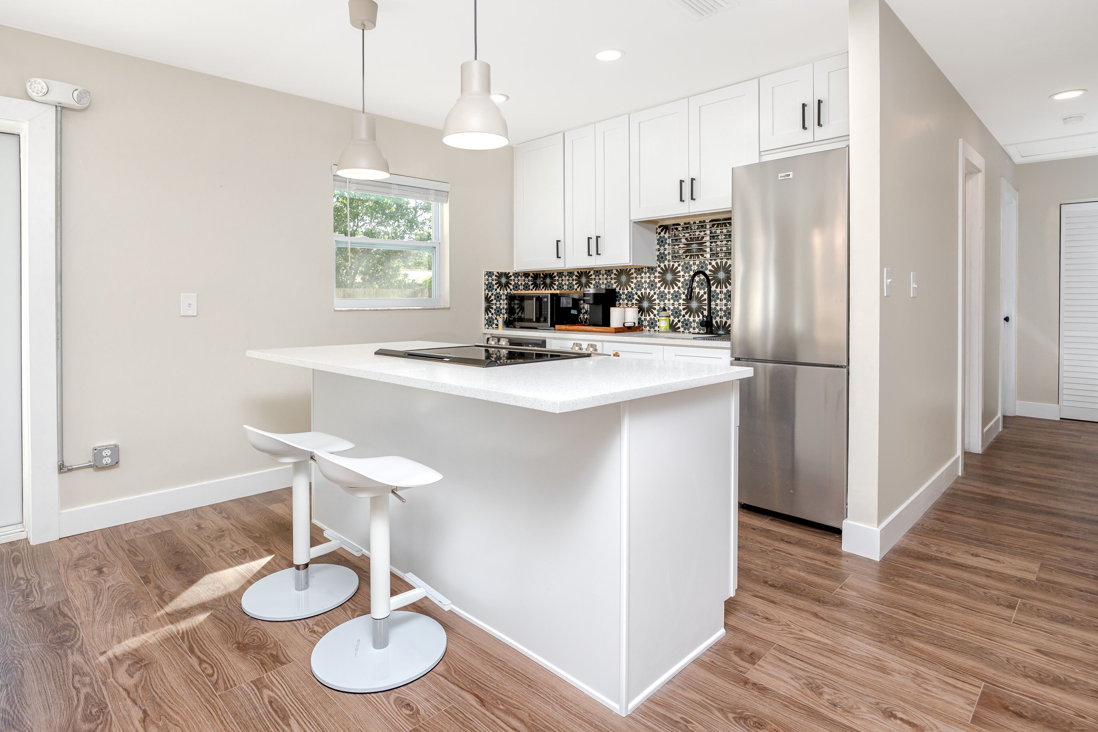 A modern kitchen with white cabinetry, a stainless steel refrigerator, and a central island with bar stools.
