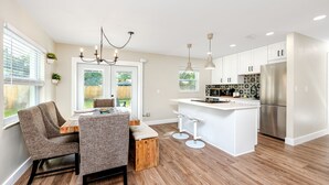 A modern kitchen with white cabinetry, a stainless steel refrigerator, and a wooden dining table with two chairs.