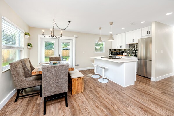 A modern kitchen with white cabinetry, a stainless steel refrigerator, and a wooden dining table with two chairs.