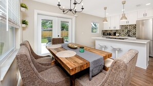 A modern kitchen with white cabinets, a stainless steel refrigerator, and a black chandelier.