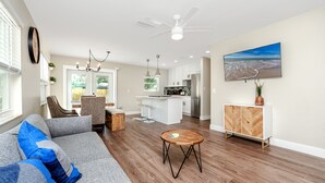 A modern living room with a gray sofa, wooden coffee table, and a kitchen area in the background.