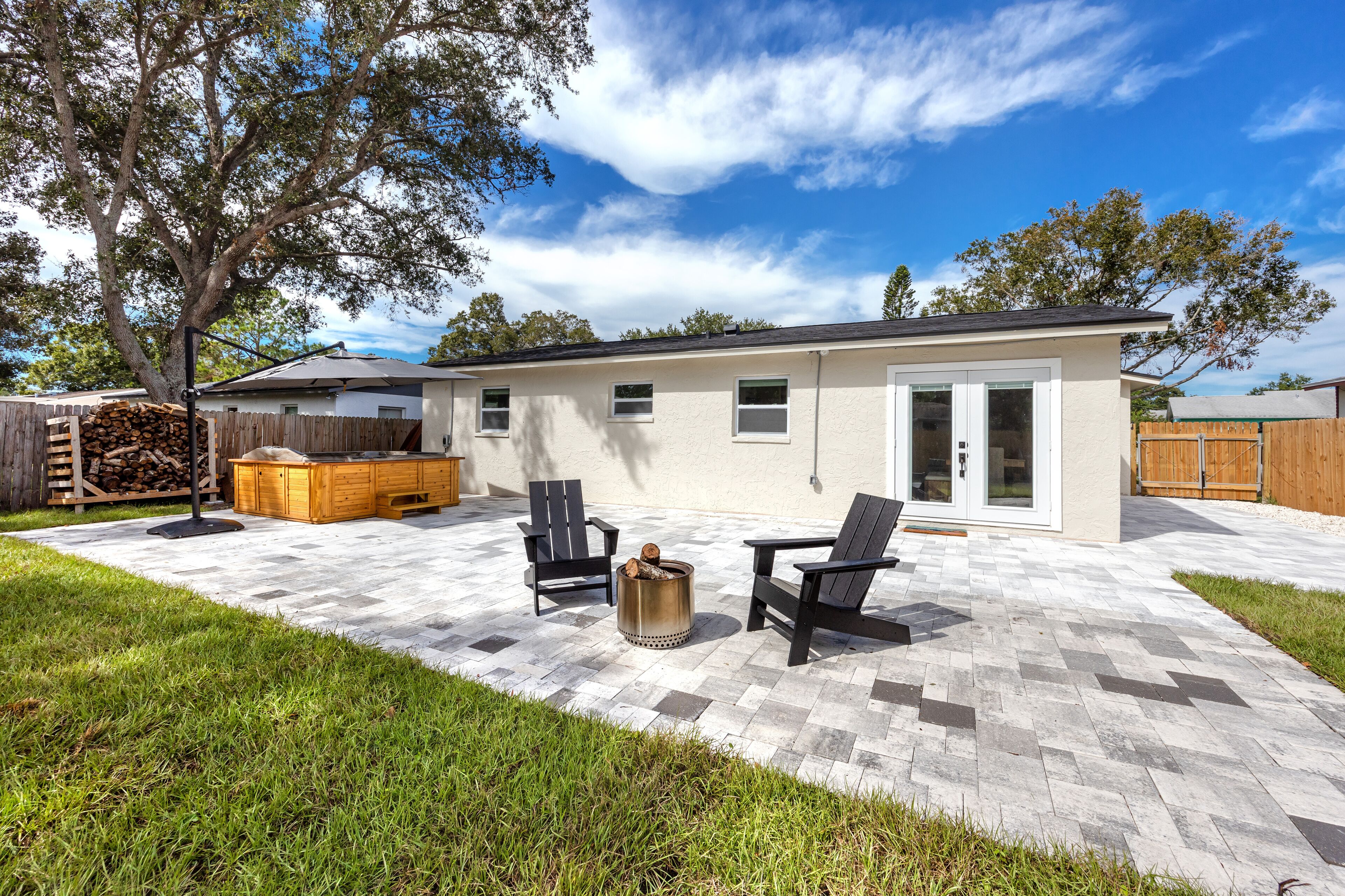 A modern house with a patio, two black chairs, a fire pit, and a wooden deck.