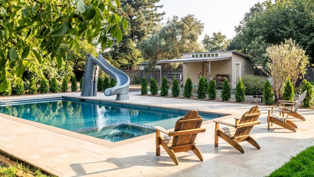 A swimming pool with a slide, surrounded by wooden chairs and a house in the background. - [Egg Farm Ranch] Heated Pool - Water Slide - Hot Tub - Dog Friendly (Kenwood)