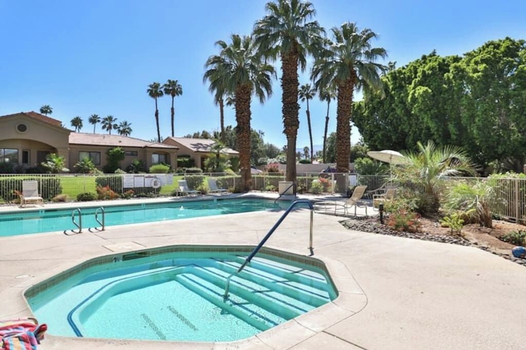 Una piscina con trampolino, circondata da palme e una recinzione.