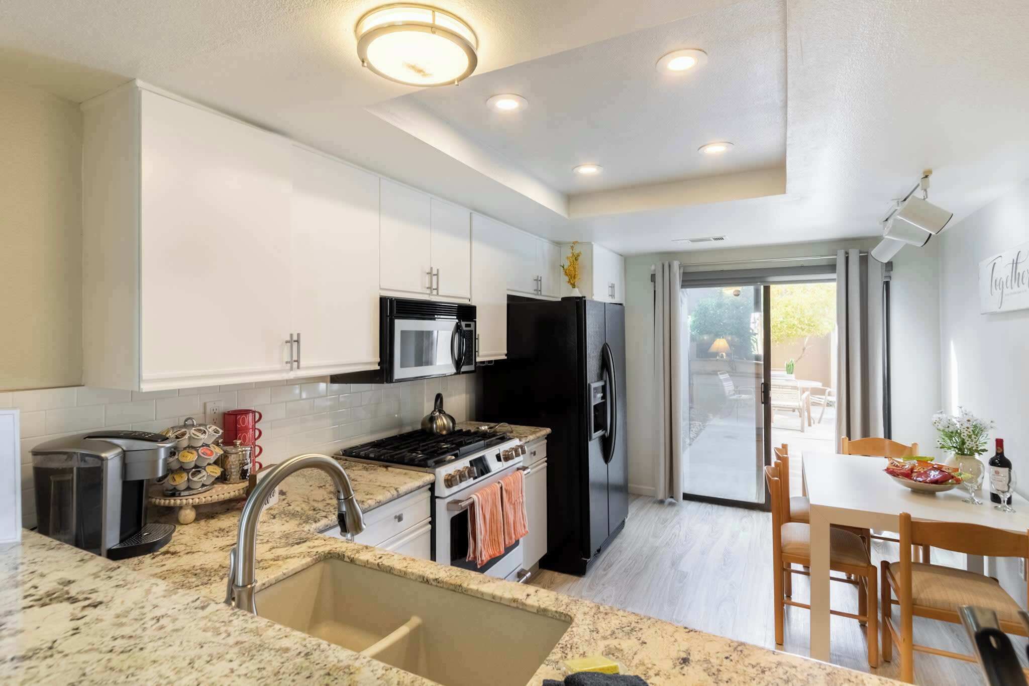 A modern kitchen with white cabinets, a black refrigerator, a stove, and a coffee maker.