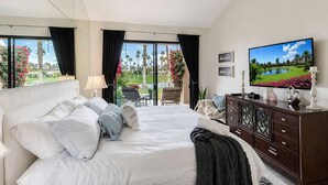 A hotel room with a large bed, a TV, a dresser, and a view of a golf course.