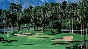 A golf course with a pond, palm trees, and mountains in the background.