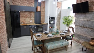 A modern kitchen with a brick wall, a dining table set for four, and a television mounted on the wall.
