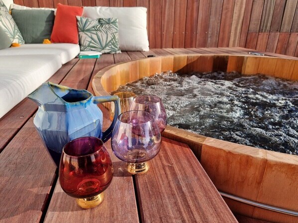 A wooden table with a hot tub, a blue pitcher, and two glass cups.