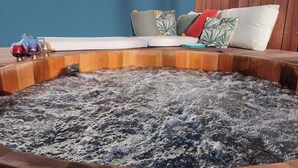 Una vasca idromassaggio con bordo in legno, una parete blu e una zona relax con cuscini.