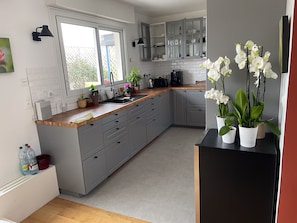 A modern kitchen with grey cabinets, a wooden countertop, and a black refrigerator.