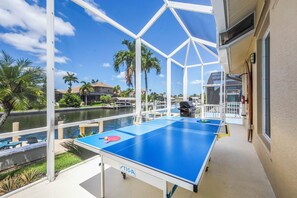 A ping pong table on a balcony with a view of a water body and palm trees. - Alluring Waterfront Home | W Exposure, Pool/Dock (Marco Island)
