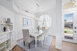 A dining area with a white table, chairs, and a chandelier. There is a window with curtains and a view of the outside. - Alluring Waterfront Home | W Exposure, Pool/Dock (Marco Island)