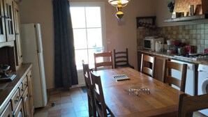 Una cocina con armarios de madera, una mesa de comedor con sillas, una lámpara colgante y una ventana con cortinas.