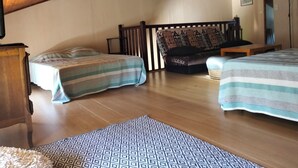 Un dormitorio con dos camas, techo de madera, alfombra estampada y sofá con cojín decorado.