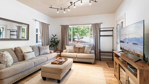 Un salon moderne avec un canapé, un pouf et un téléviseur posé sur un meuble en bois.