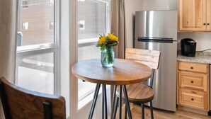 Une petite cuisine avec une table ronde en bois, une chaise, un vase avec des fleurs, un réfrigérateur et des placards en bois.