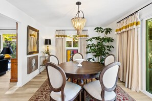 Un comedor con una mesa redonda de madera, seis sillas, una araña y una planta grande.