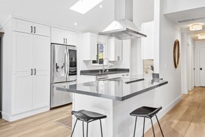 Una cocina moderna con armarios blancos, un refrigerador de acero inoxidable, una isla grande con taburetes de bar y un tragaluz.