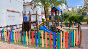 A playground with a slide and climbing structures, surrounded by a colorful fence. - Ola Azul Bungalow V (Benidorm)